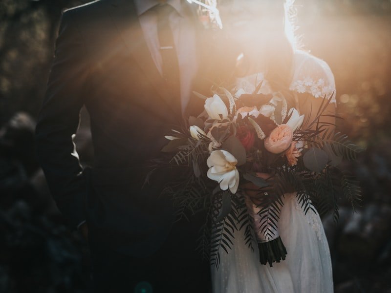 Wedding bouquet of white and burgundy florals held by a couple at sunset