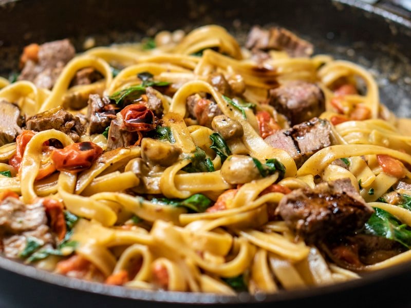 Tagliatelle pasta with mushrooms, beef, and herbs in a pan