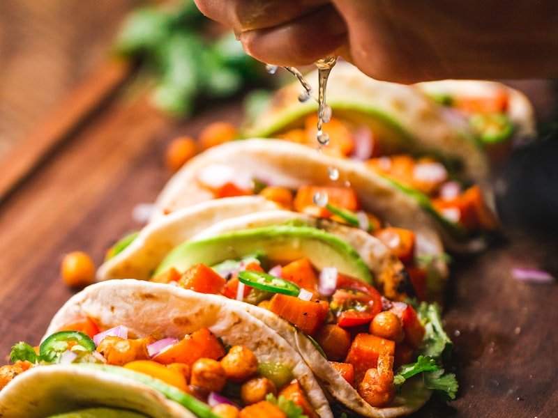 Row of soft tacos with chickpeas, vegetables, and lime on wood board