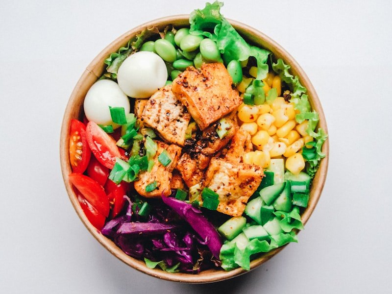 Boxed individual lunch meal with grilled protein, salad, and corn in a bowl